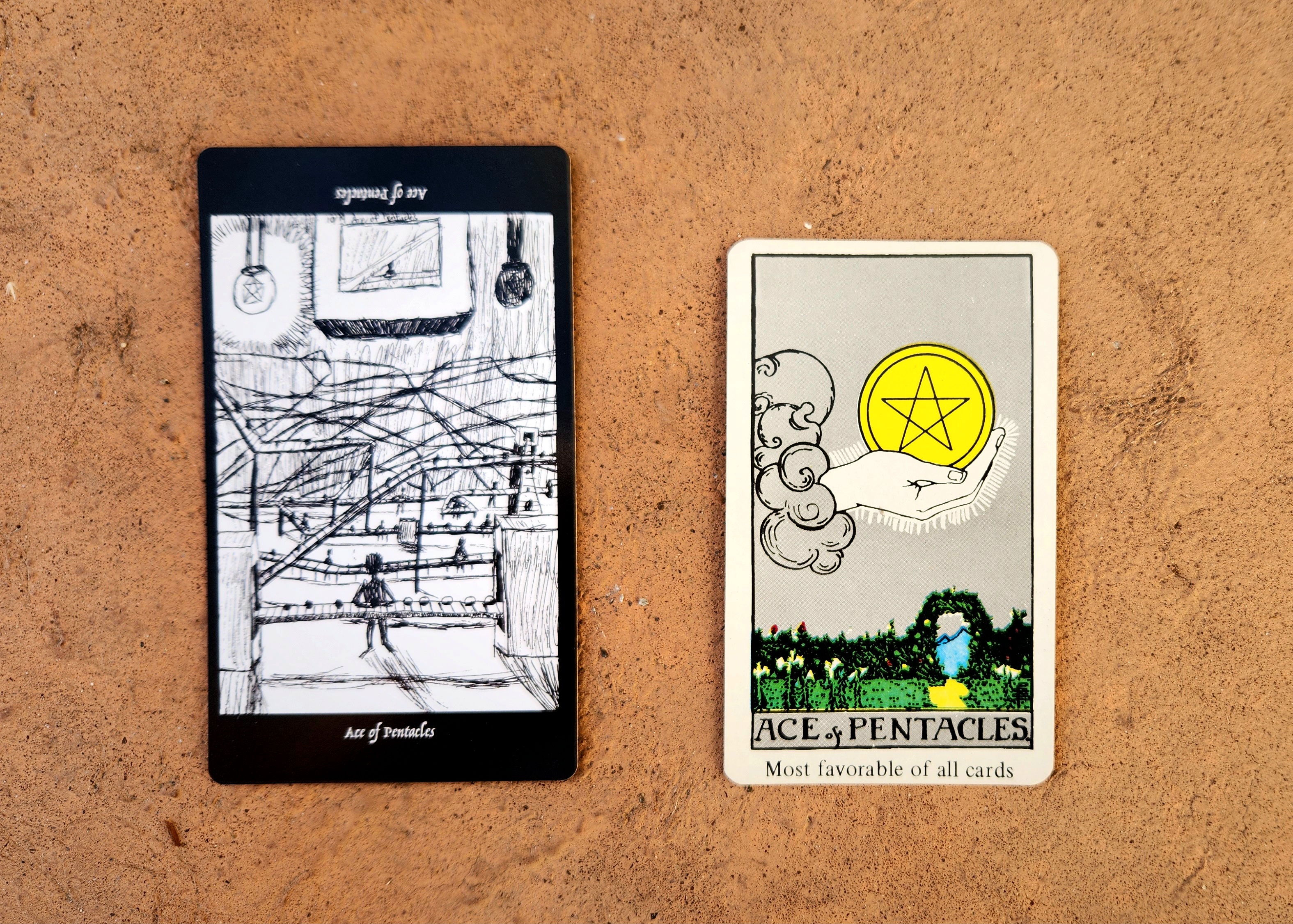 The Ace of Pentacles from the Elsewhere Tarot, showing a rough, sketchy drawing of a convoluted assembly line with a human figure turning half dark objects into dark objects, alongside the Ace of Pentacles from a janky, bootleg RWS deck, showing a hand emerging from a cloud with the offer of a pentacle coin in the sky above a garden path with a floral arch leading to a mountain.